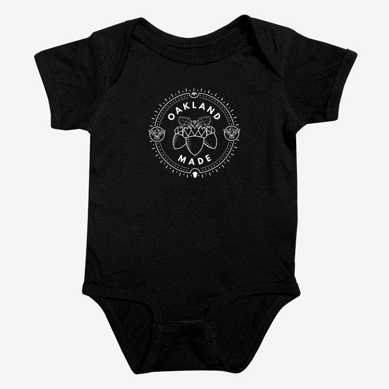 Black infant one-piece with a white circle graphic with the words “Oakland Made” and hand-drawn chestnuts. 