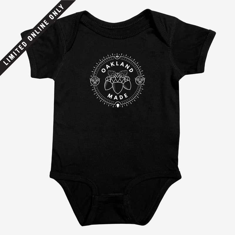 Black infant one-piece with a white circle graphic with the words “Oakland Made” and hand-drawn chestnuts. 