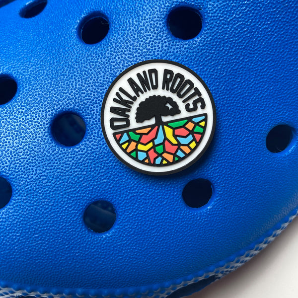 Close up of full-color Roots SC full-color logo shoe charm on a blue croc sandle.