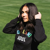 Woman on a soccer field wearing a black hoodie with OAKLAND SOUL wordmark on the chest.