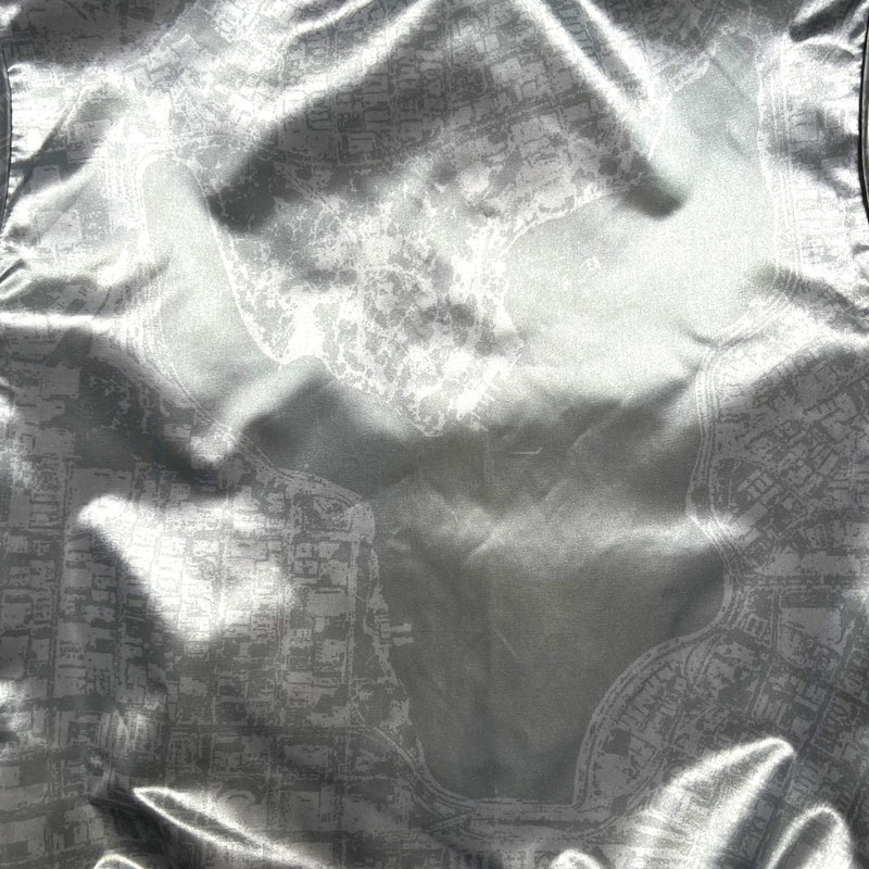 Detailed close-up of the silver reverse side of a satin jacket, imprinted with an aerial map of Oakland.
