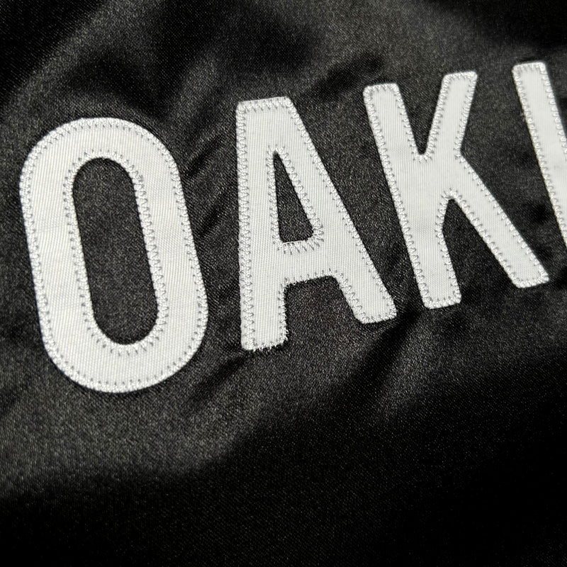 Detailed close-up of OAK letters in Oaklandish wordmark on a black satin reversible jacket.