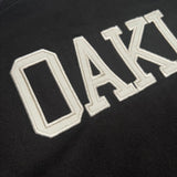 Detailed close-up OAK wordmark applique on the back of a black cadet jacket.