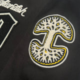 Detailed close-up of 3-dimensional white and yellow chenille Oaklandish logo patch on the sleeve of a black cadet jacket.
