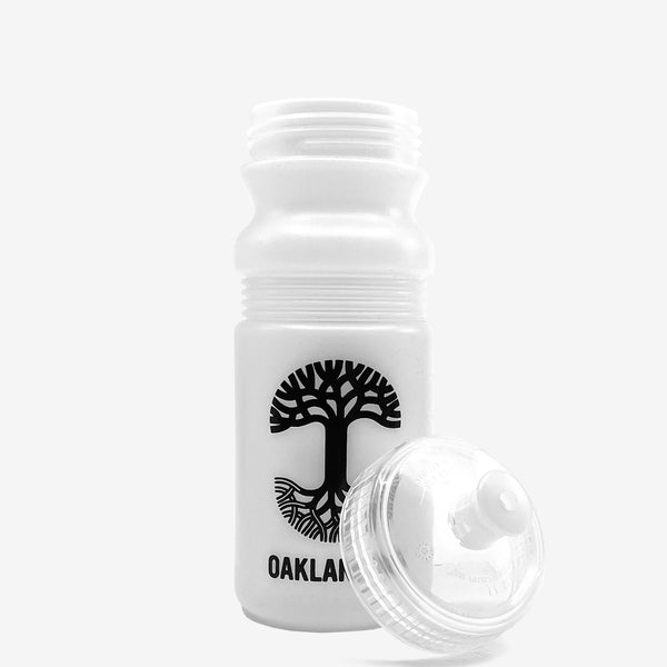 Unscrewed frost white bicycle water bottle with a black Oaklandish tree logo and wordmark .