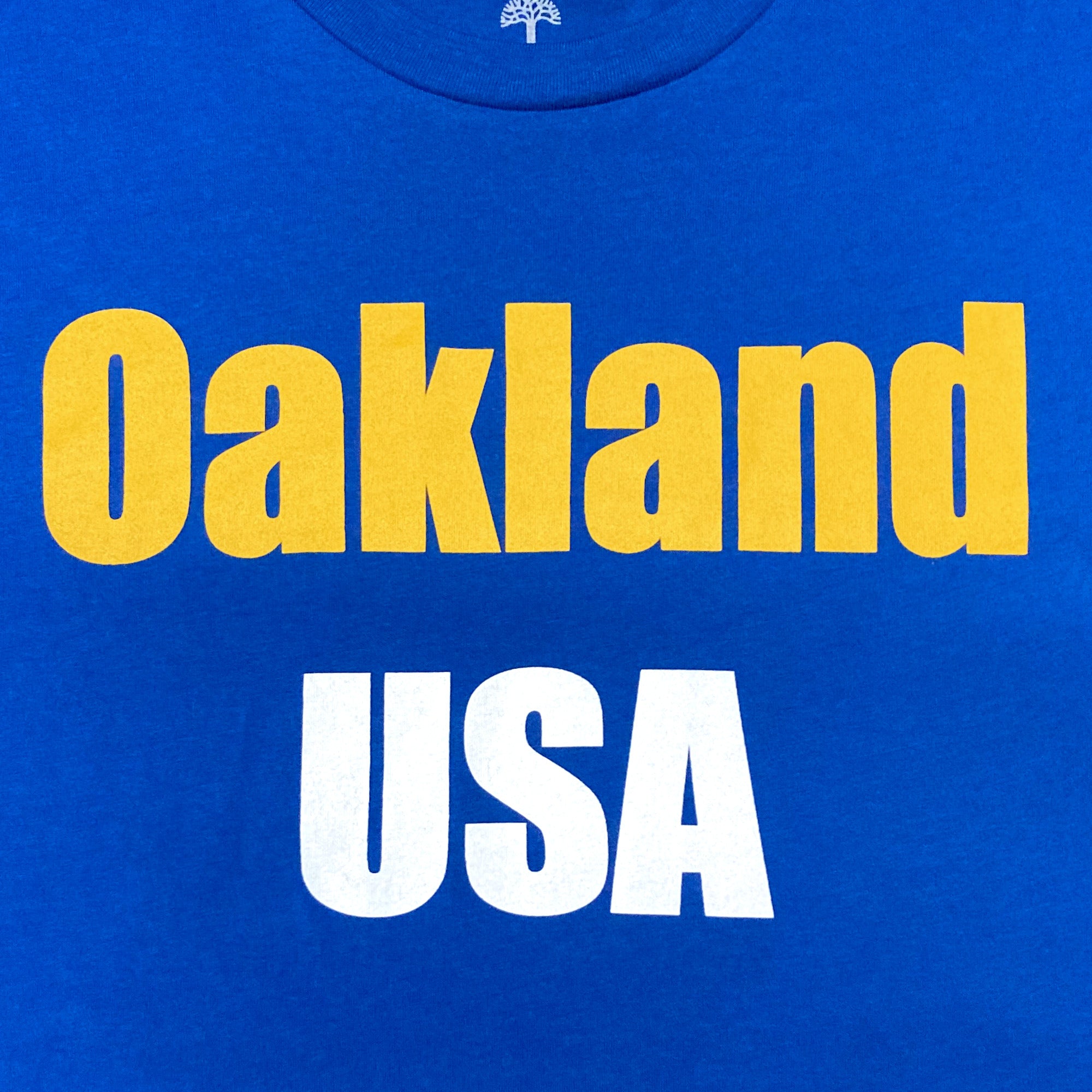 Detailed close-up image of Royal t-shirt with 'Oakland USA' wordmark across chest.