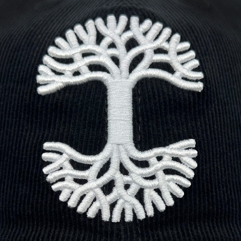 Detailed close-up of embroidered white Oaklandish tree logo on a black Mitchell & Ness cap.