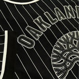Detailed close-up of large black and white Oaklandish tree logo and wordmark applique on the back of black baseball jersey.