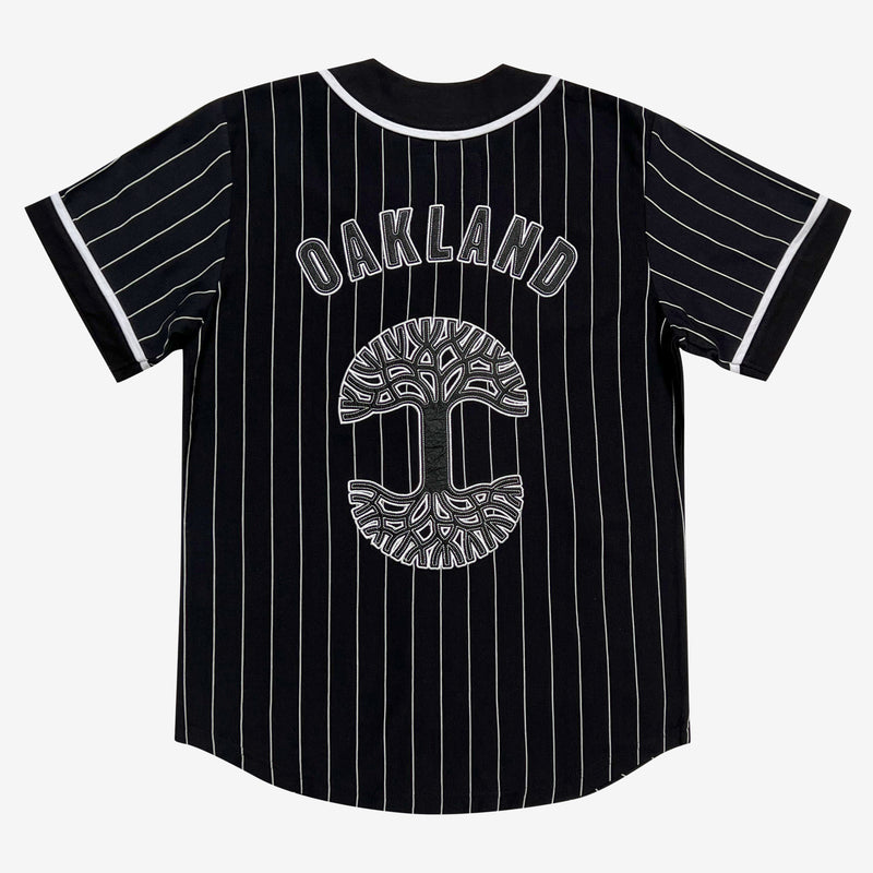 The backside of a black baseball jersey large black and white Oaklandish tree logo and wordmark applique.