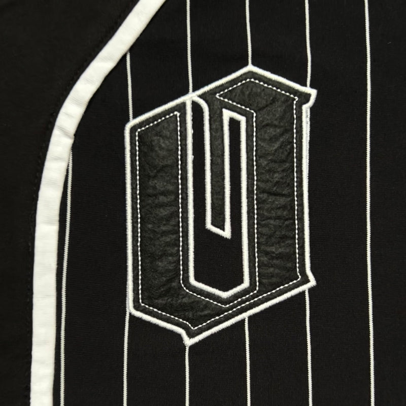 Close-up of black and white O for Oakland applique on the chest of a black baseball jersey with white stripes.