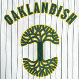 Detailed close-up of a large green and yellow Oaklandish tree logo and wordmark applique on a white baseball jersey.