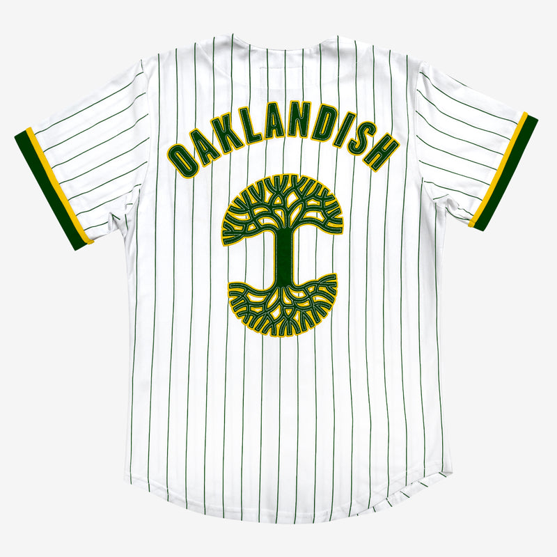 Backside of white baseball jersey with a large green and yellow Oaklandish tree logo and wordmark applique.