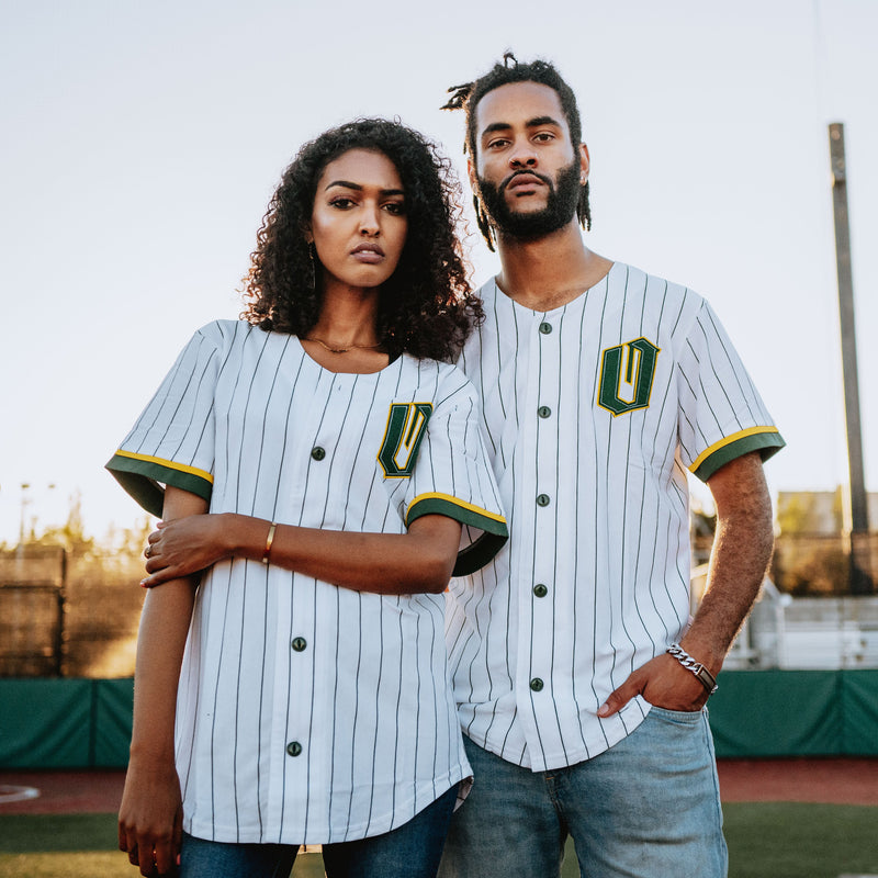 Man and woman on a baseball field in green striped white baseball jerseys with green and gold O for Oakland applique on the chests.
