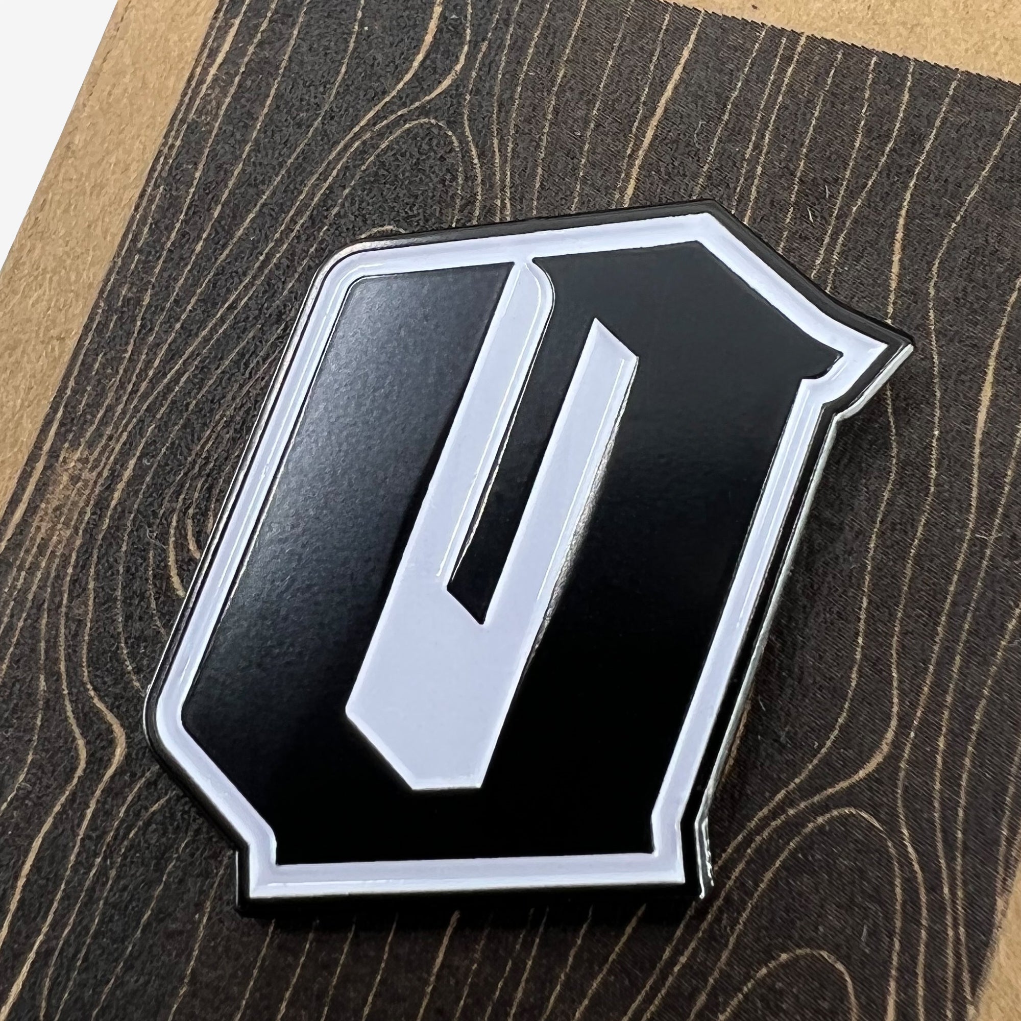 Close up of a black and white enamel lapel pin with Official O for Oakland on brown paper Oaklandish retail packaging.