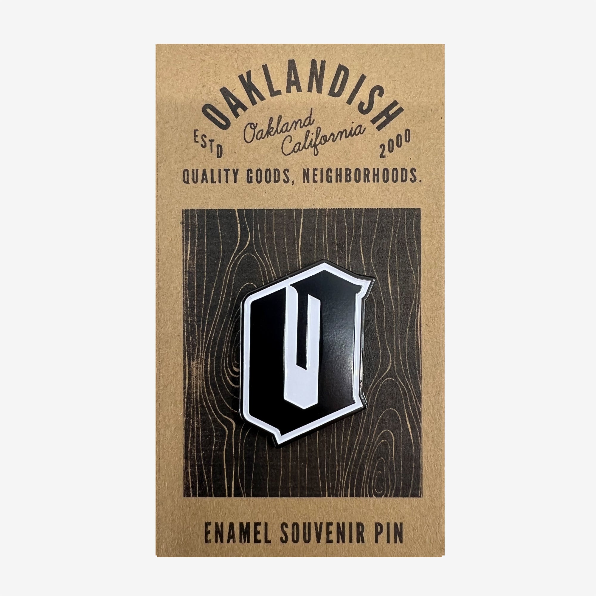 A black and white enamel lapel pin with O for Oakland on brown paper retail packaging with the words Enamel Souvenir Pin. 