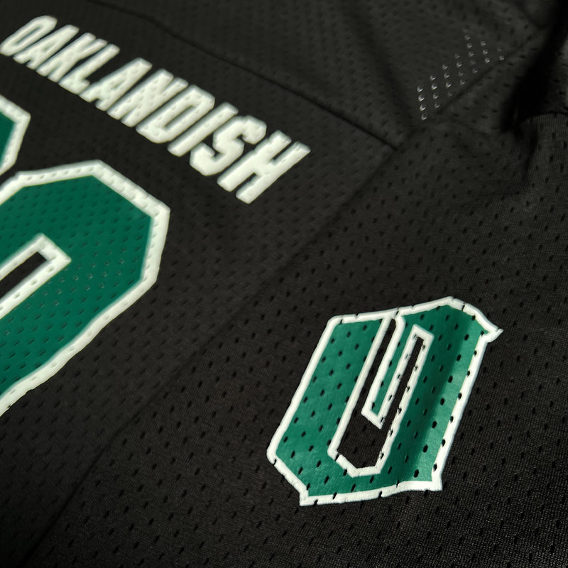 Close-up of a green O for Oakland with a white outline on the sleeve of a black mesh football jersey.