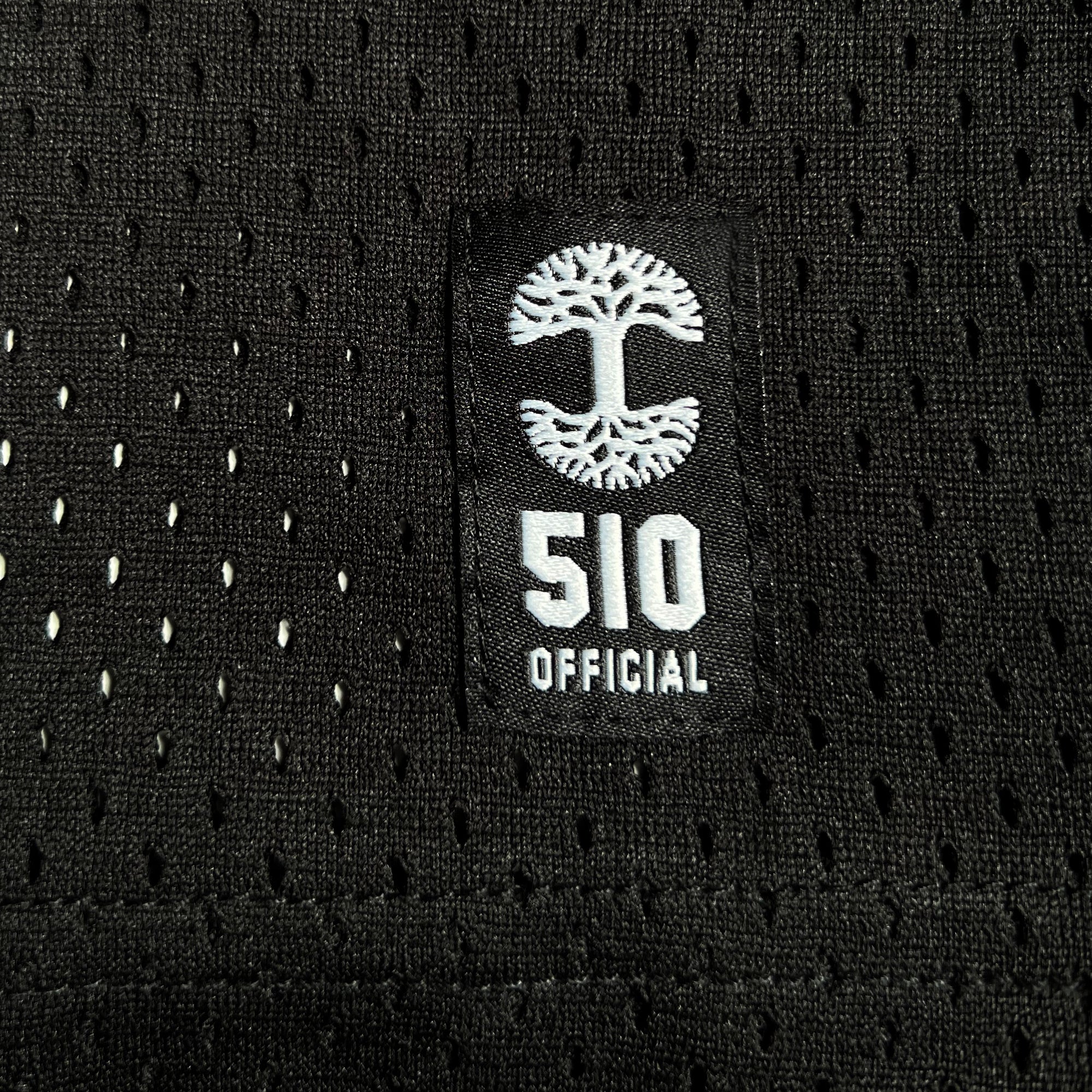 A close-up of the Official Football Home Jersey shows black mesh fabric with small holes, featuring a black rectangular patch. The patch displays a white tree in a circle above "510 OFFICIAL," highlighting its Oaklandish style from the brand Other.