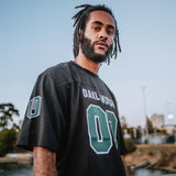 A man wearing a black mesh football jersey with 00 green numbers and a large white Oaklandish wordmark.