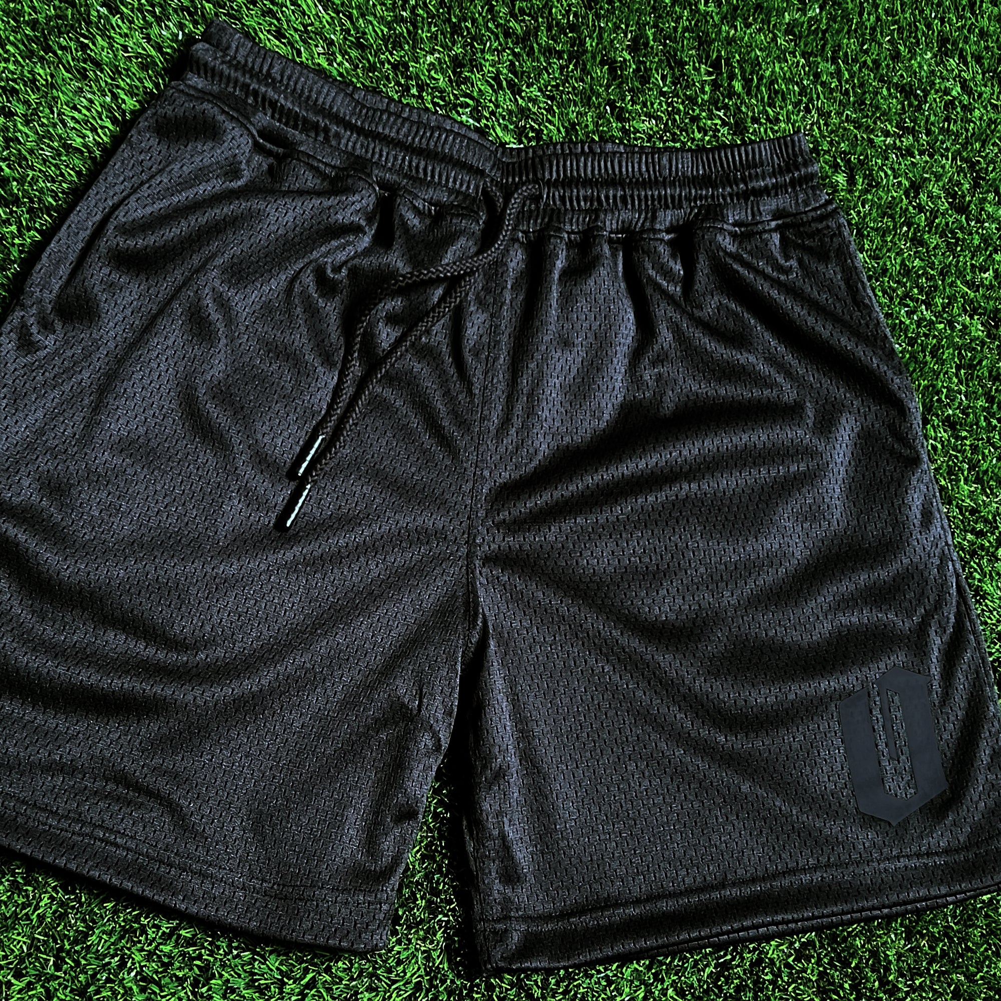 Men’s black mesh athletic shorts with O for Oakland Official logo on the bottom of left leg on green grass. 