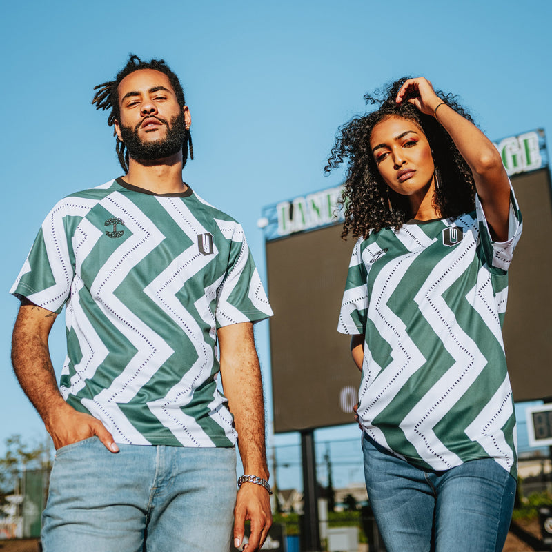 Man and woman outdoors in soccer jerseys with green and white zig-zag patterns.