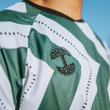 Close-up of embroidered black Oaklandish tree logo on green and white zig-zag patterned soccer jersey. 
