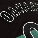 Detailed close-up of OAKLAND OO applique on black and green soccer jersey.