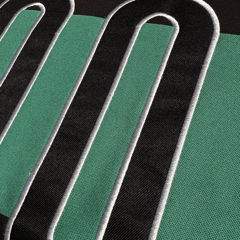 Detailed close-up of OO applique on black and green soccer jersey.