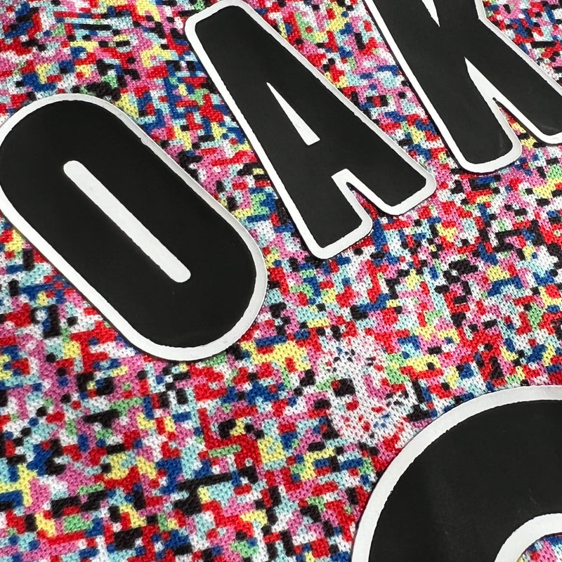 Detailed close-up of half of OAKLAND wordmark on multi-colored speckled soccer jersey.