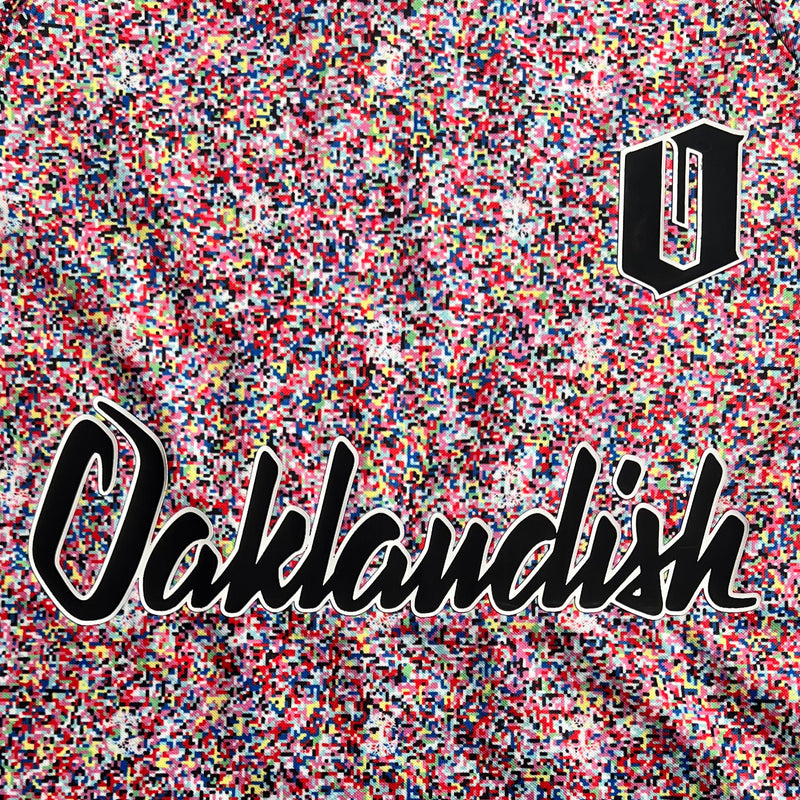 Close-up of multi-colored speckled soccer shirt with cursive Oaklandish wordmark and black O for Oakland applique.