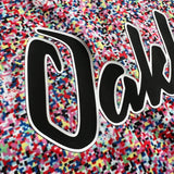Detailed close-up of half of the cursive OAKLAND wordmark on multi-colored speckled soccer jersey.