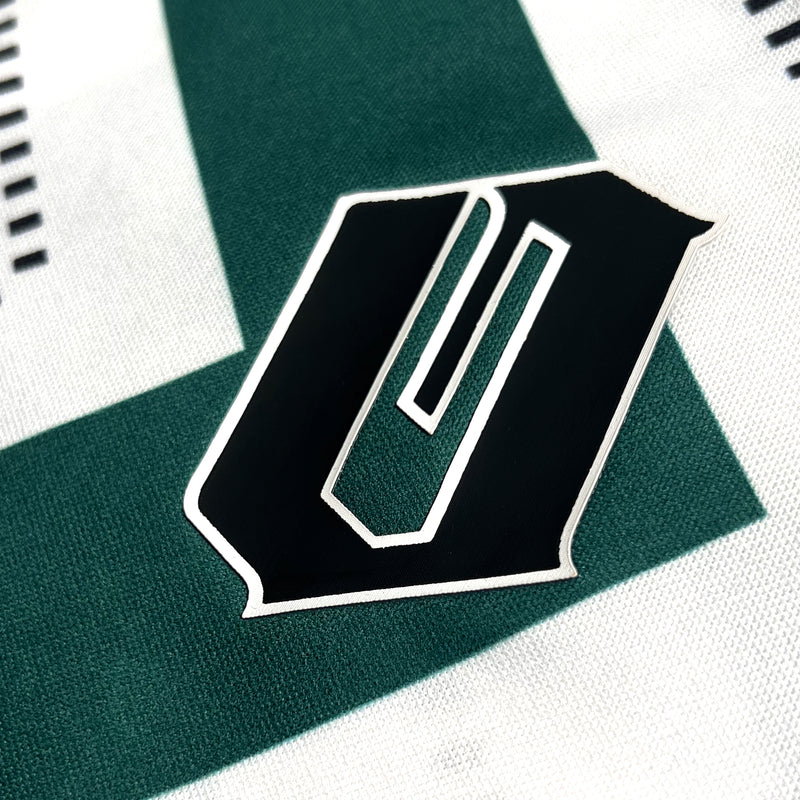 Close-up of black Oakland O on green and white soccer jersey chest.