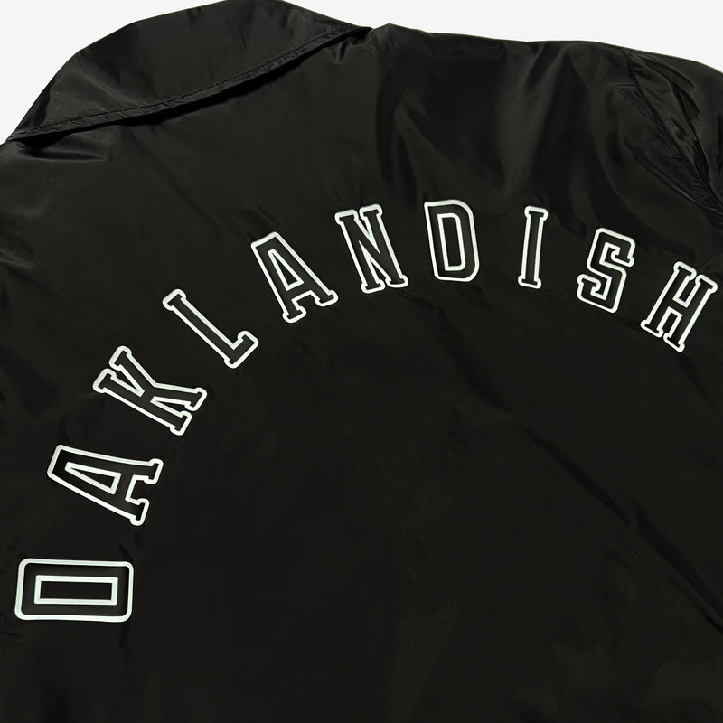 Close up of back side of black nylon coaches jacket with Oaklandish wordmark.