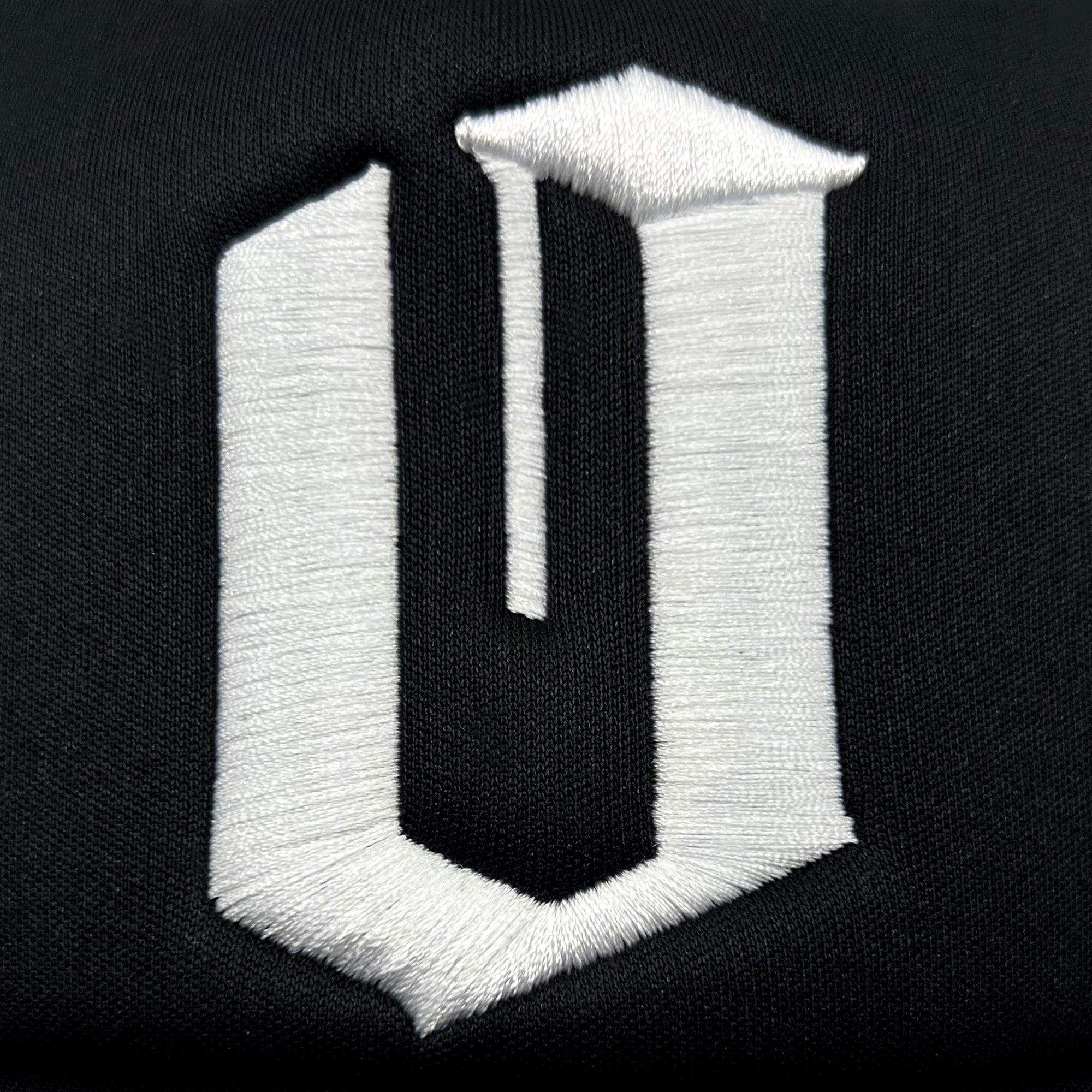 The image features a stylized, embroidered letter "U" in white thread on a black fabric background. It has a three-dimensional appearance with sharp, clean edges, similar to the bold and striking contrasts typical of Oaklandish's Official O Trucker hats.