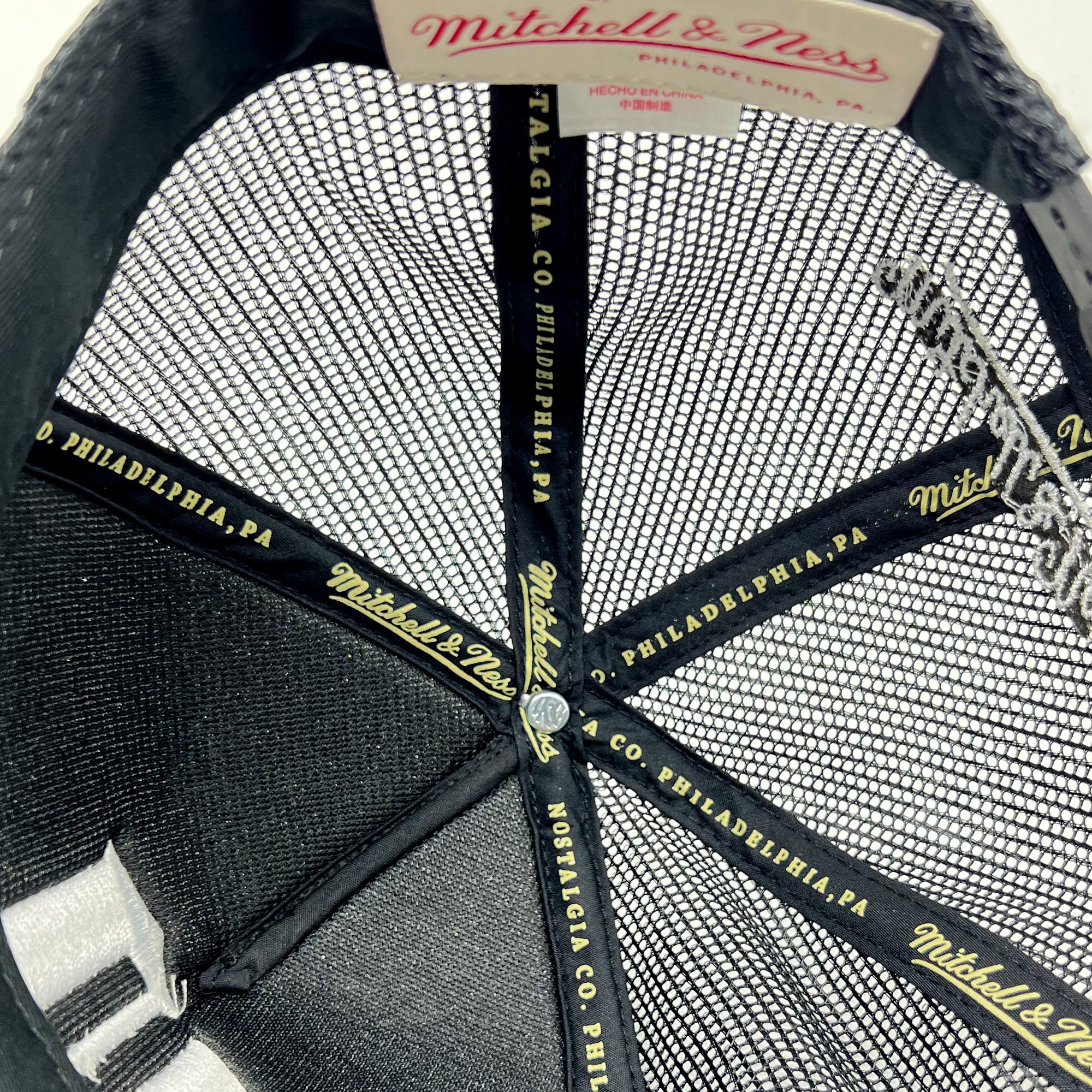 Detailed close-up of Mitchell & Ness taping inside the crown of a black truckers cap.