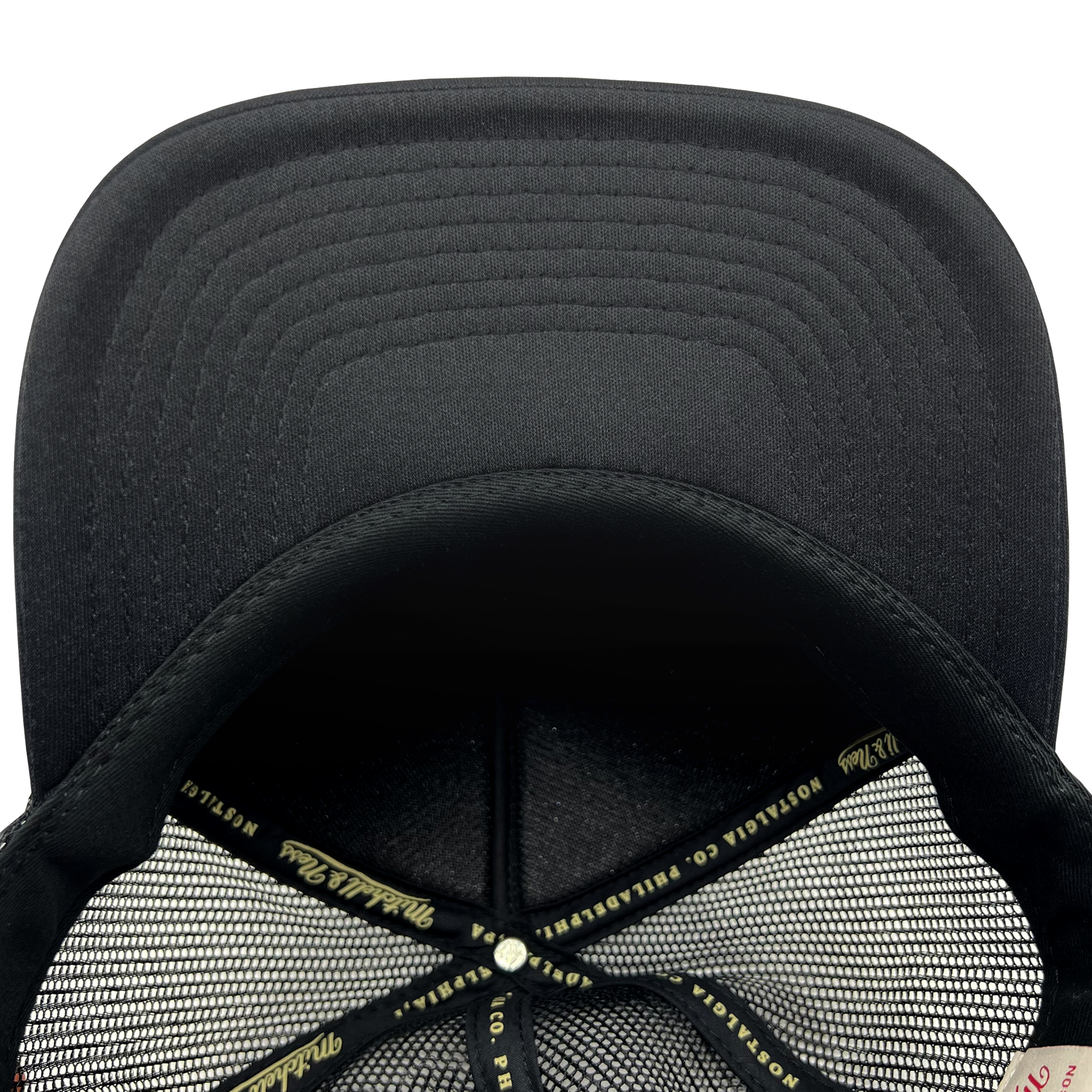 Close-up view of the interior of a black Official O Trucker baseball cap by Oaklandish. The inside features a mesh lining with crosshatched stitching and a central button. The cap has fabric labeled "PIPILA" and other branding on the inner band that runs around the base. The brim shows reinforced stitching.