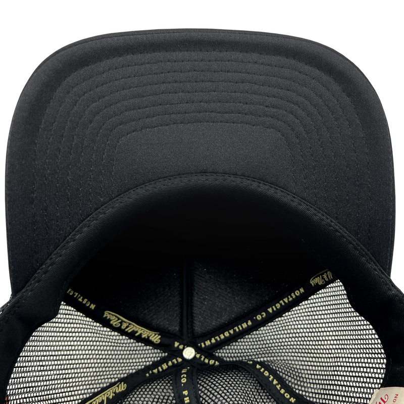 Detailed close-up of black undervisor and taping inside the crown of a black Mitchell & Ness truckers cap.