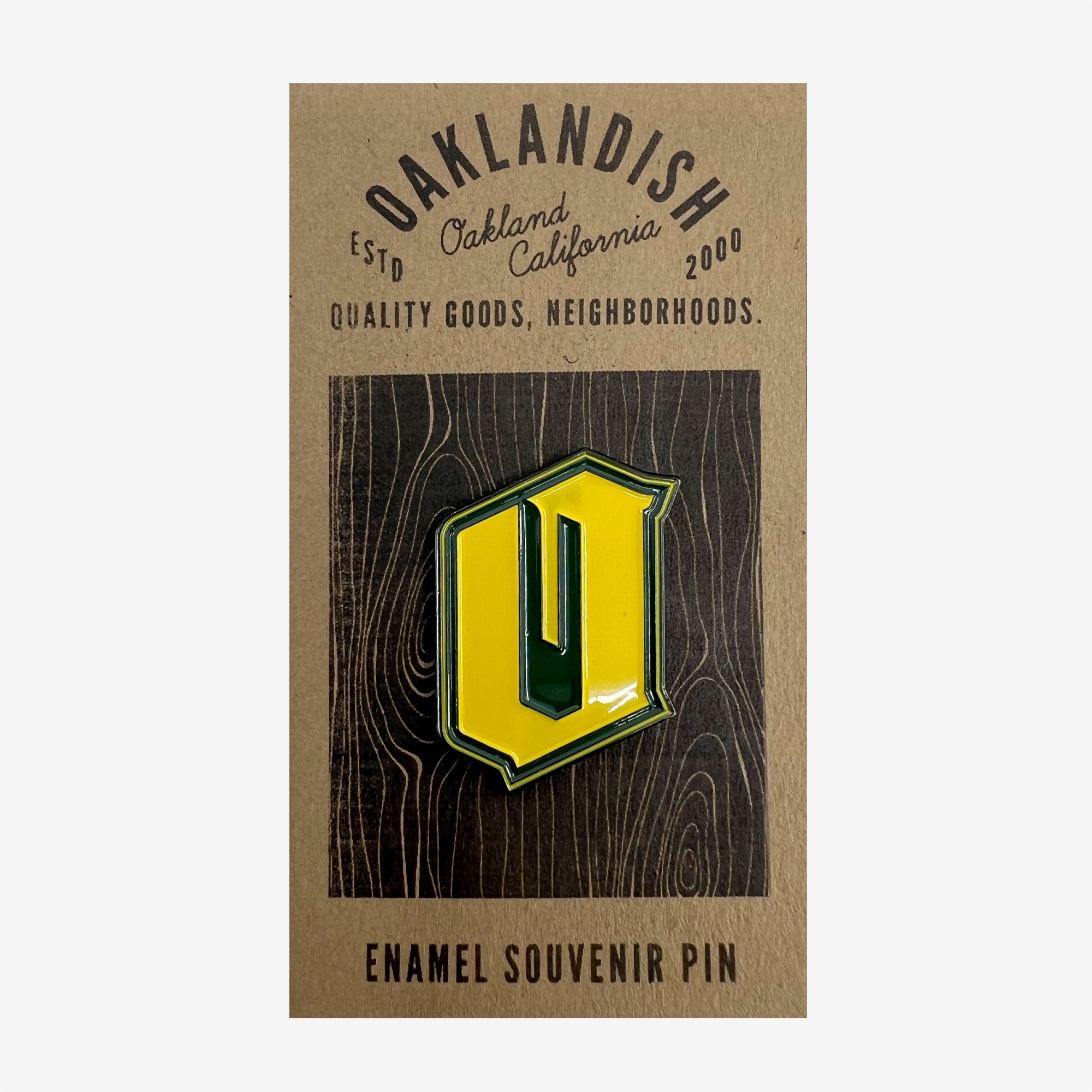 Green and yellow enamel lapel pin with Official O for Oakland on brown paper Oaklandish retail packaging.