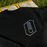 Close-up of a black and white O for Oakland applique patch on the chest of a black crewneck sweatshirt lying on the grass.