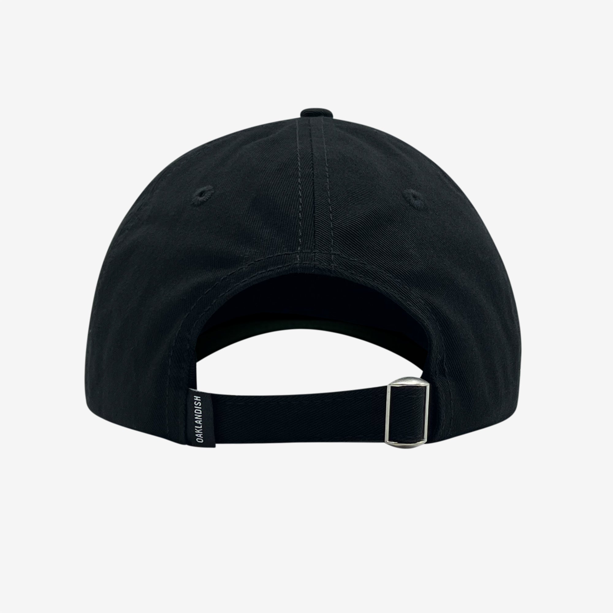 Rear view of the Official Micro Logo Dad Hat by Oaklandish in black. The cap features a central seam with visible stitching, an embroidered "O" on the side, a metal buckle on an adjustable strap, and a small rectangular tag with text on the left side of the strap. The white background highlights the cap's intricate details.