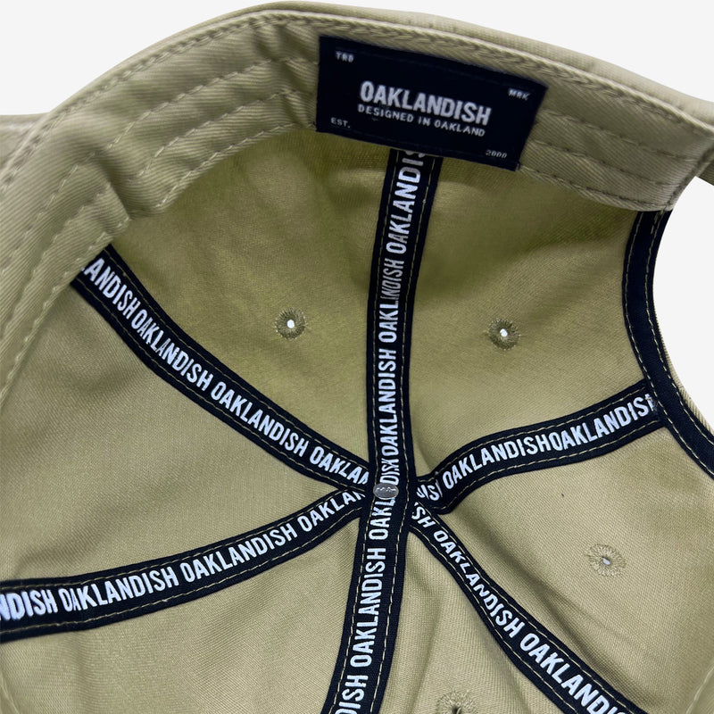 Inside of khaki dad hat crown with ‘OAKLANDISH’ wordmark on black striping and Oaklandish patch.