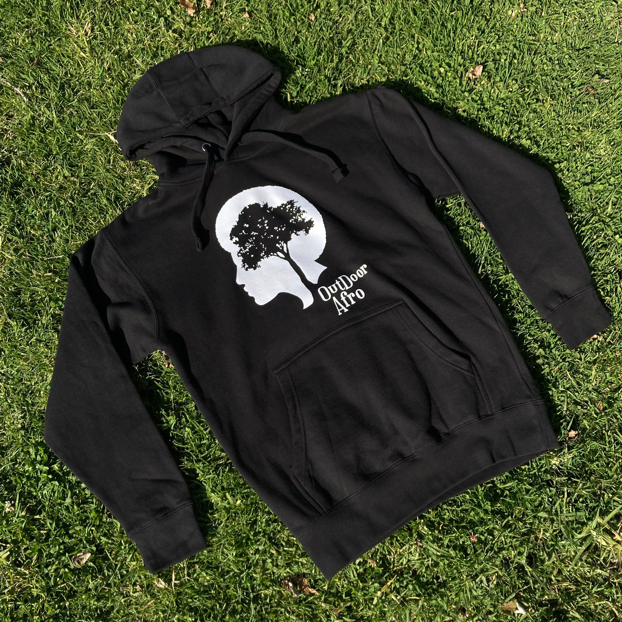 Black hoodie with OutDoor Afro logo and wordmark lying outdoors on grass.