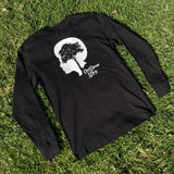 Black long-sleeve t-shirt with white OutDoor Afro logo and wordmark lying outdoors on grass.