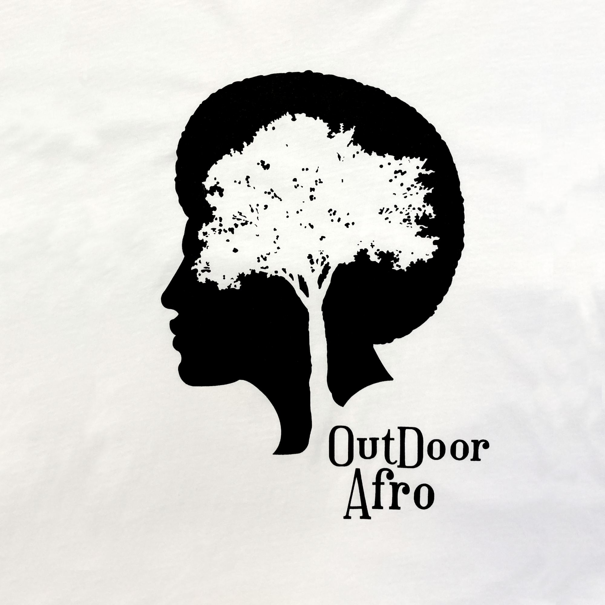 The "Outdoor Afro Signature Tee" by Partner features a unique graphic with a black silhouette of a woman's face in profile, where her hair transforms into an intricate tree with branches and leaves. To the right of the silhouette, the text "Outdoor Afro" is prominently displayed in black lettering against a white background, making it an ideal choice for an outdoor-themed t-shirt.