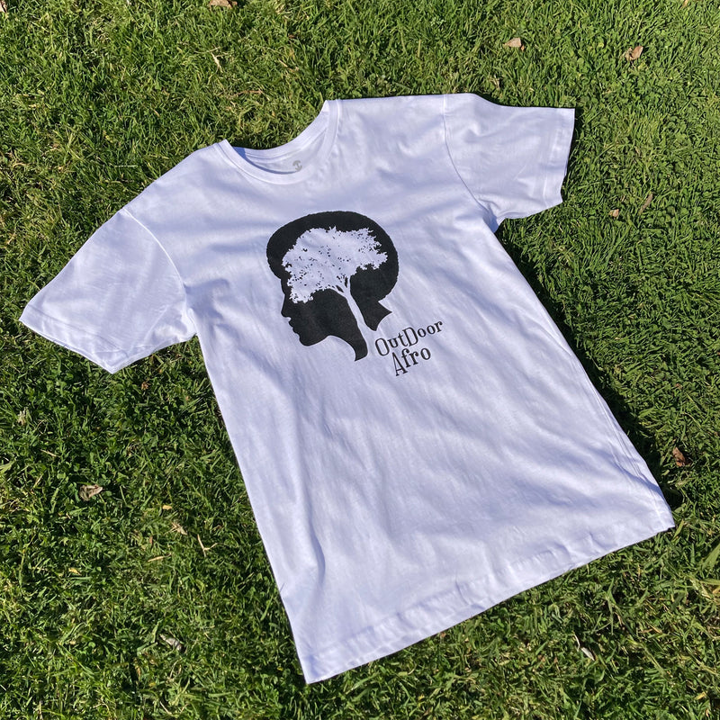 White t-shirt with black OutDoor Afro logo and wordmark lying outdoors on grass.