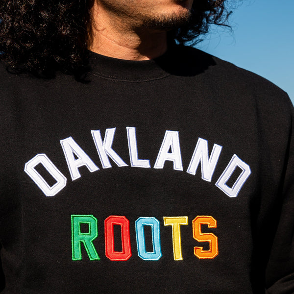 Close-up of white “OAKLAND” applique wordmark and full-color “ROOTS” wordmark underneath on a man’s chest.