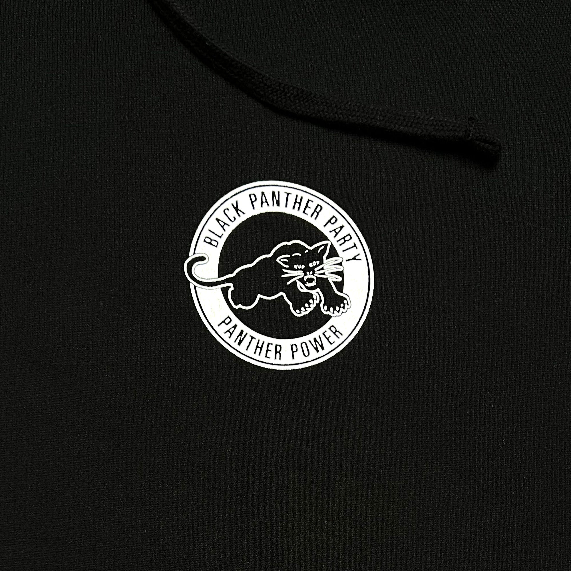 Close-up of the Black Panther Power Hoodie by Oaklandish. This black pullover hoodie features a circular logo in white, displaying an illustration of a black panther ready to pounce. The text "Black Panther Party" arches over the panther, while "Black Panther Power" is inscribed below. The logo is centrally positioned on the hoodie.