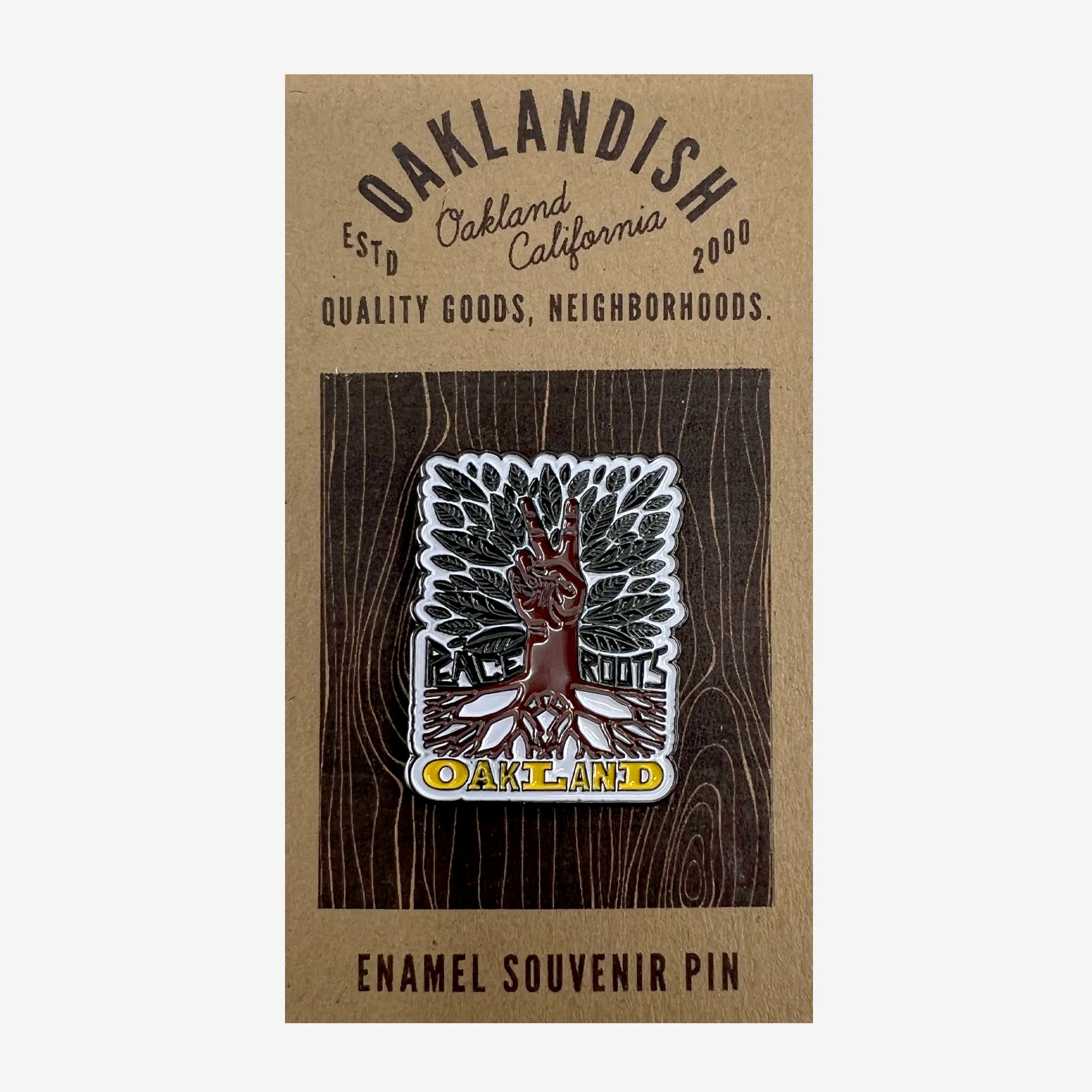Enamel pin with yellow Oaklandish wordmark, brown roots, peace sign hand, green leaves, and Peace and Roots on retail packaging.