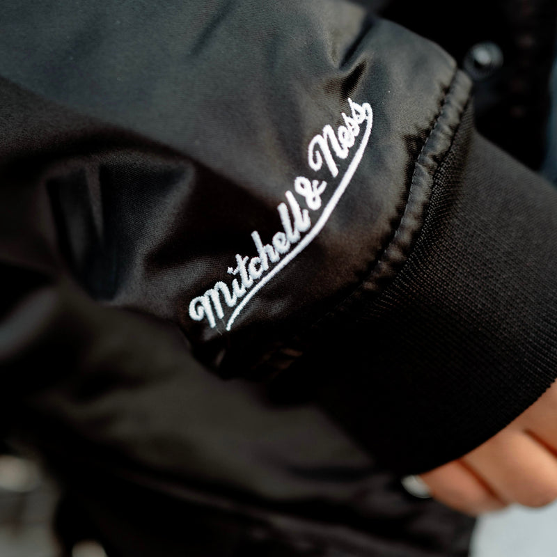 Close-up of Mitchell & Ness wordmark on a striped satin jacket sleeve.