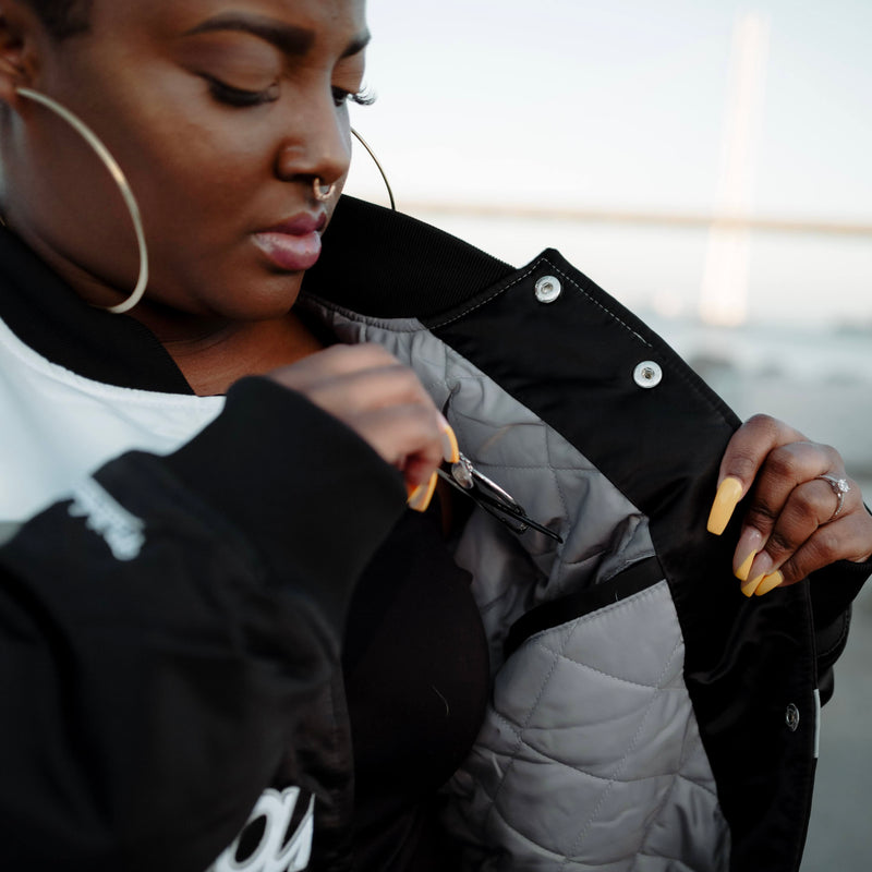 Close-up of a woman reaching into the inside pocket of a striped heavyweight satin jacket. 