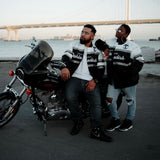 Man & woman on a motorbike wearing striped satin jackets with a California Oaklandish wordmark and Oaklandish tree logo.